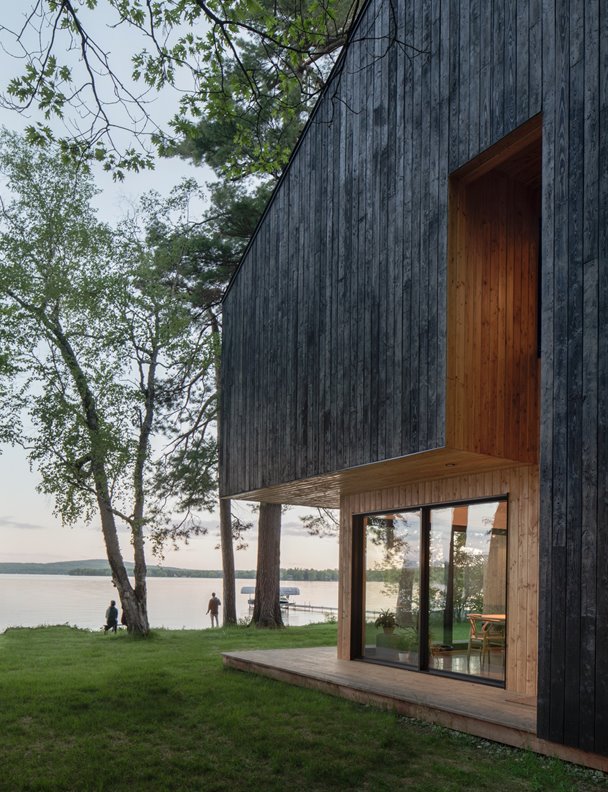 Una moderna cabaña de madera negra proyectada junto a un lago