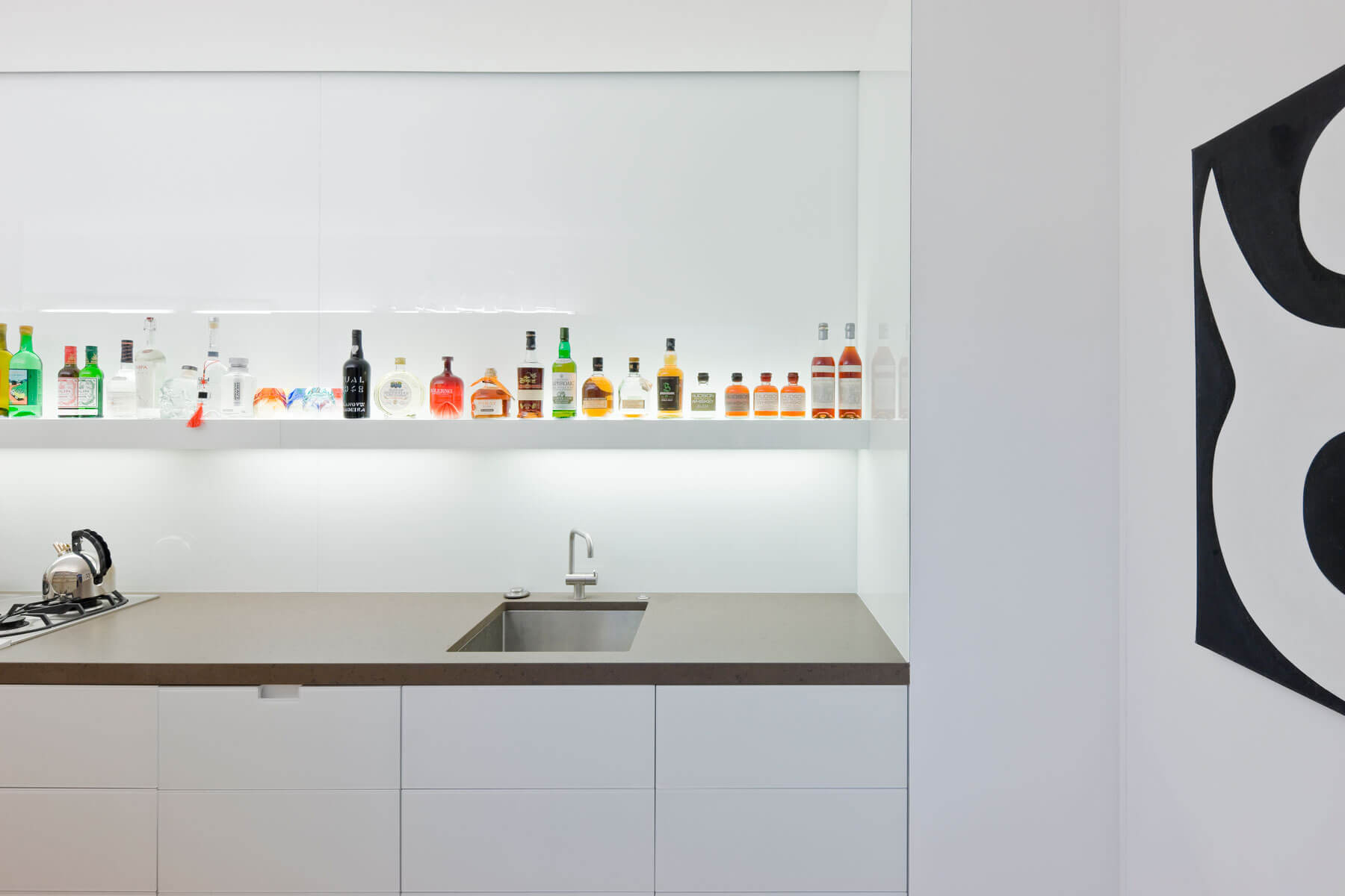 11. En contraste con el resto del espacio presidido por la curva, en este espacio de uso ocasional para la preparación de alimentos la línea recta es la protagonista. Un escueto anaquel blanco se inunda de color con las bebidas