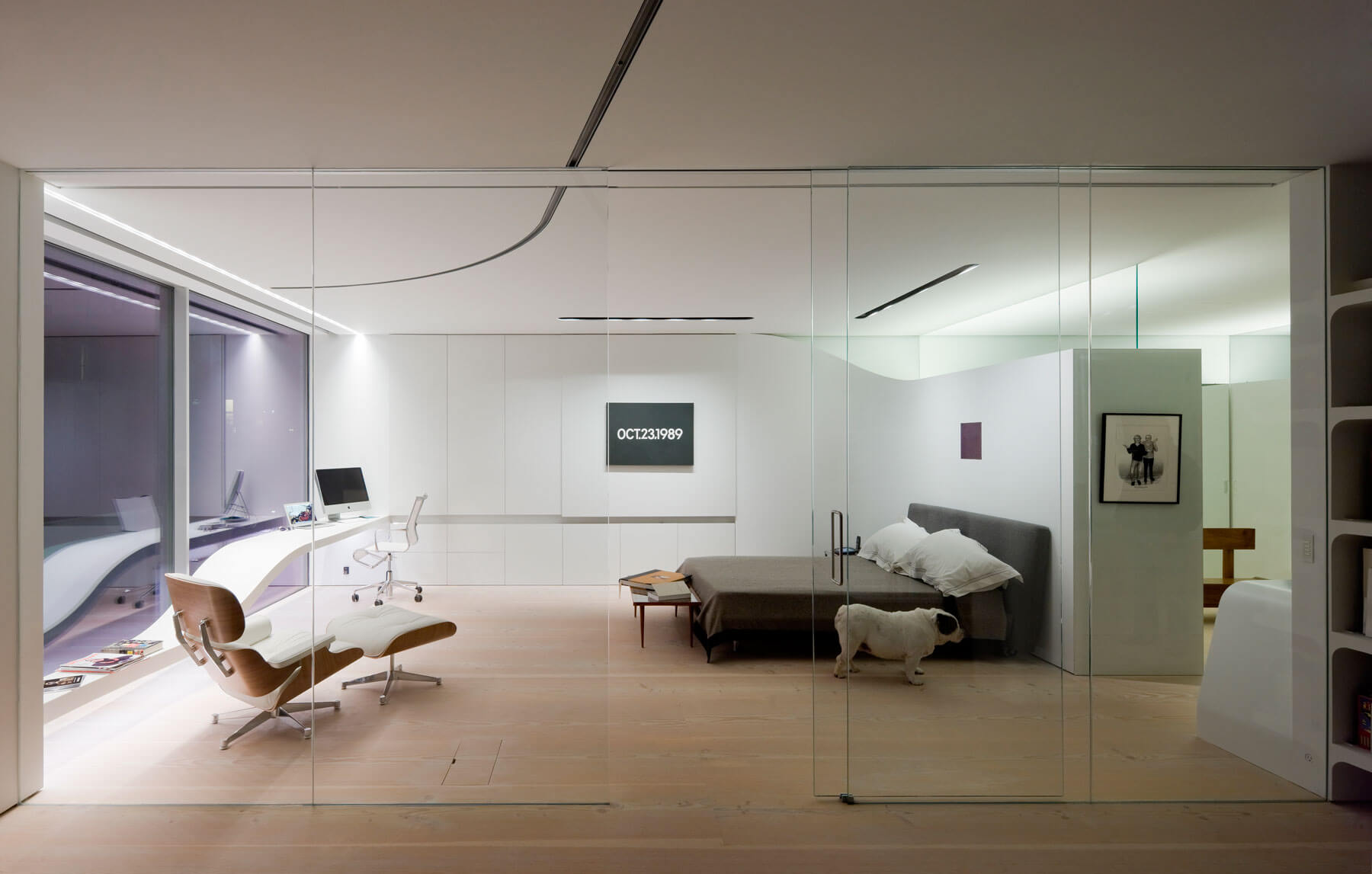 12. La zona de noche se abre al exterior con una gran cristalera ante la que se ha situado una mesa de trabajo ondulada. Tras la cama en encuentra un espacioso vestidor con superficies lacadas de color blanco