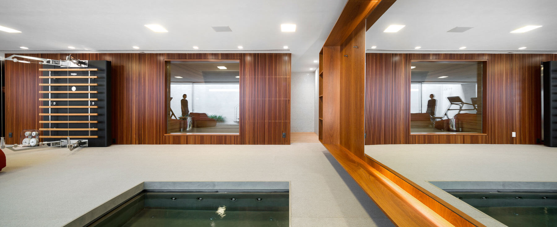 28. Al lado del garaje se ubica el gimnasio, un espacio que no abandona la marcada línea de la casa con módulos separadores de madera que incorporan un gran espejo. Junto al gimnasio está integrado una sauna diseñada en madera por Studio MK27, abierta a la sala de fitness gracias a un gran cristal