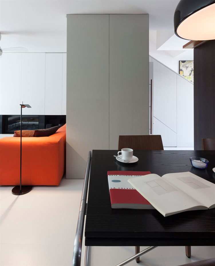 marbella8. En la zona de estar, un único sofá con alegre tapicería naranja es el contrapunto cromático de toda la vivienda en la que el color blanco y la madera oscura son los grandes protagonistas