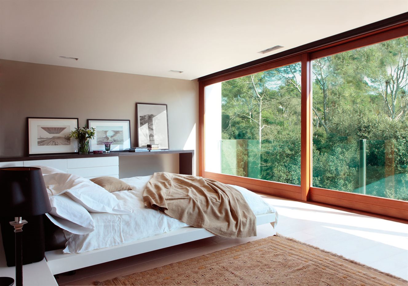 Dormitorio con amplias ventanas de madera y cuadros apoyados junto a la pared 