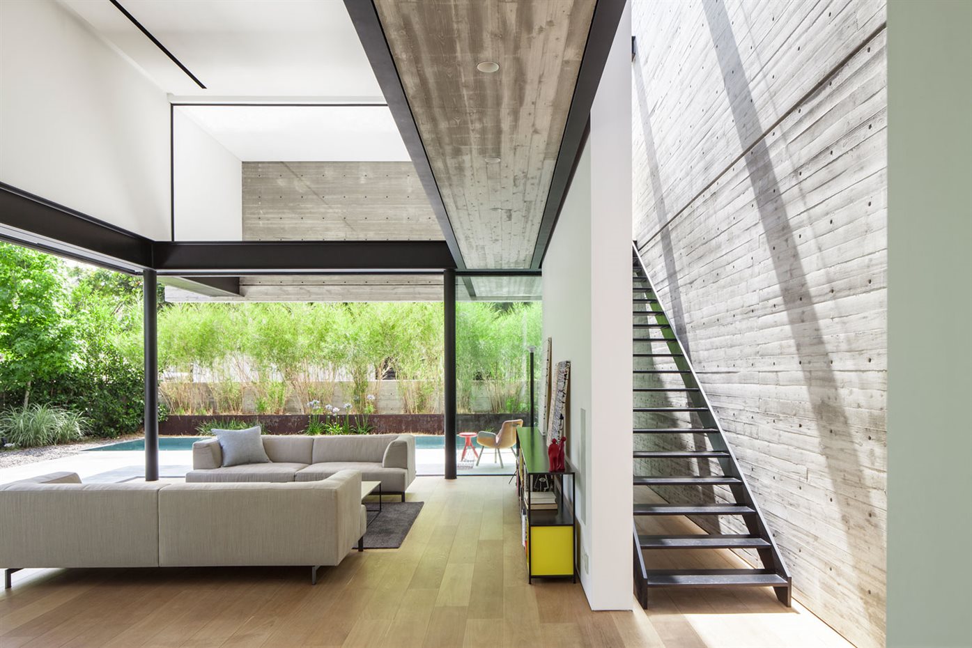 SHAIBEL HOUSE 027. El espacio del salón es un ambiente a doble altura totalmente acristalado y abierto al jardín.La escalera, una escueta estructura de hierro pintado, se esconde entre la sensual pared de hormigón iluminado de forma cenital y una pared blanca del salón. Los sofás son de Piero Lissoni
