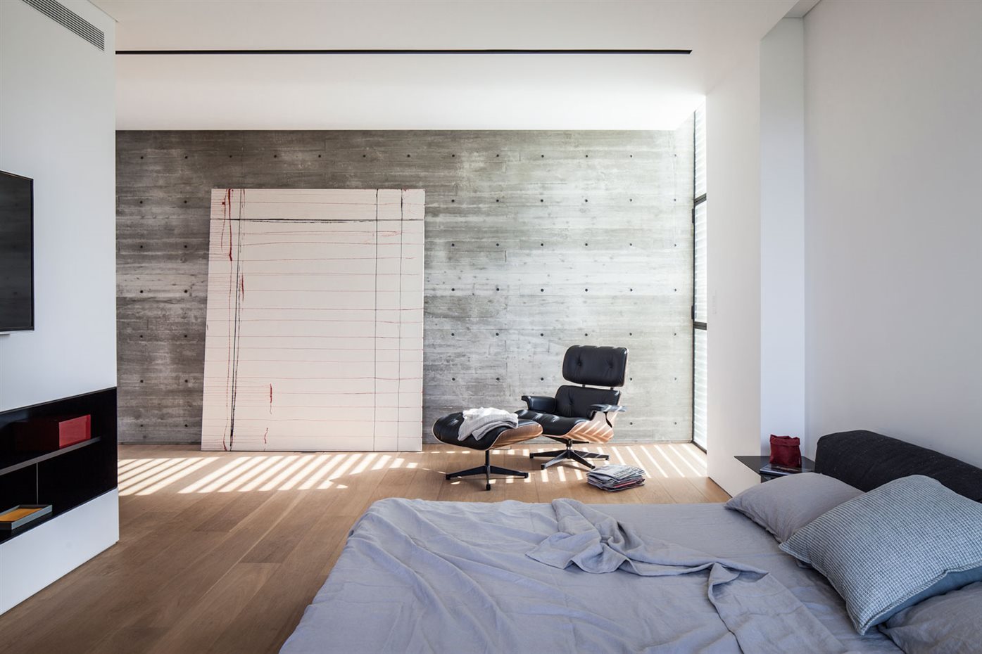 SHAIBEL HOUSE 057. Ubicado en la segunda planta, el dormitorio principal es un espacio reposado con suelo de lama ancha de madera y paredes de hormigón. Cama, de Cassina y butaca de Vitra
