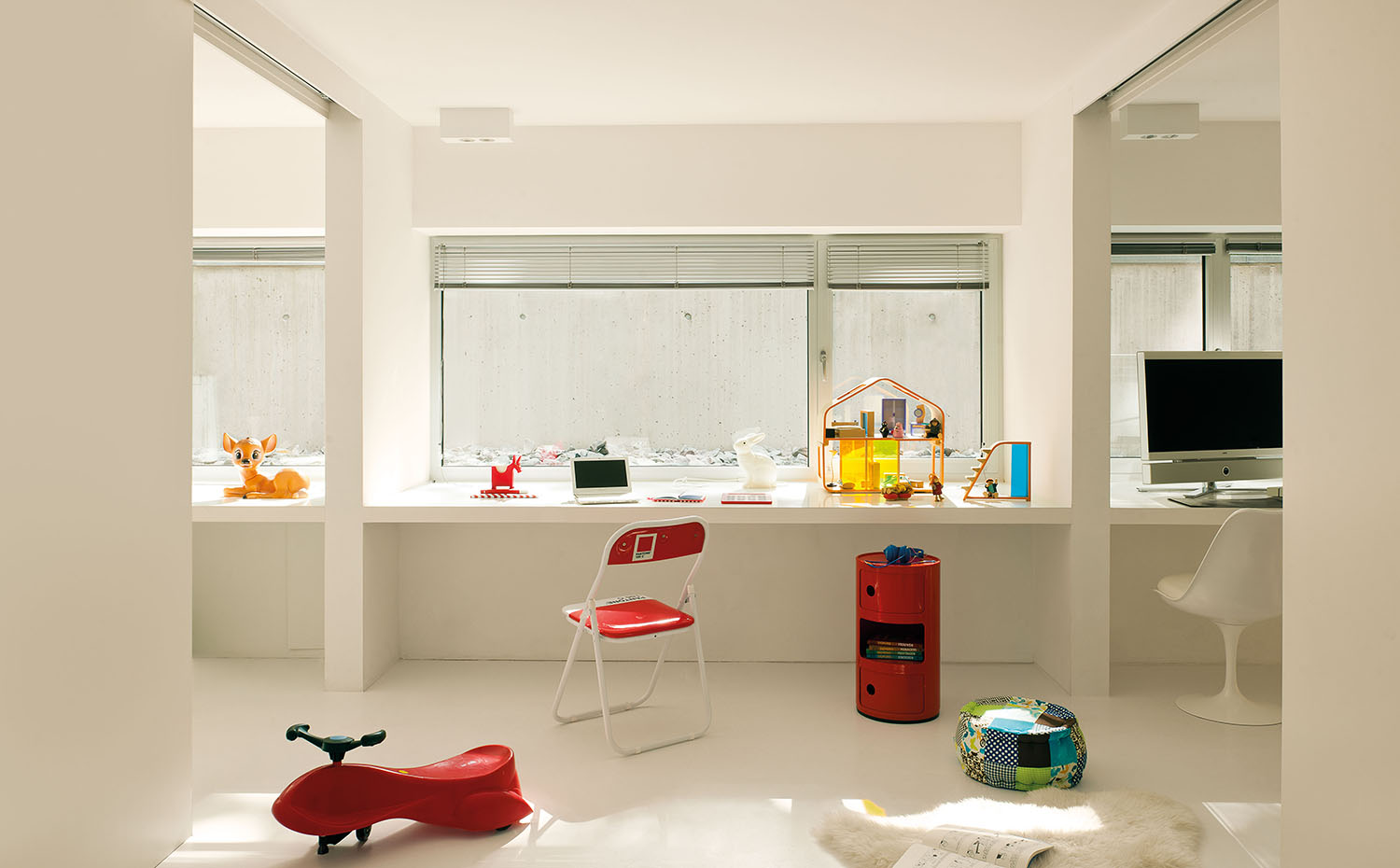 En la habitación infantil, silla Pantone 186C. Mesa auxiliar roja con ruedas Componibili, diseño de Anna Castelli Ferrieri para Kartell. Puf de la firma Rice