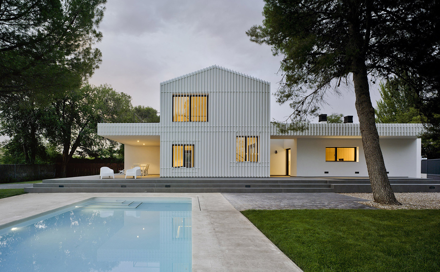 CASA F&A (2). El volumen principal recurre a la imagen prototípica de la casa con cubierta a dos aguas, pero matizada por la celosía metálica que actúa como una segunda piel protectora del sol