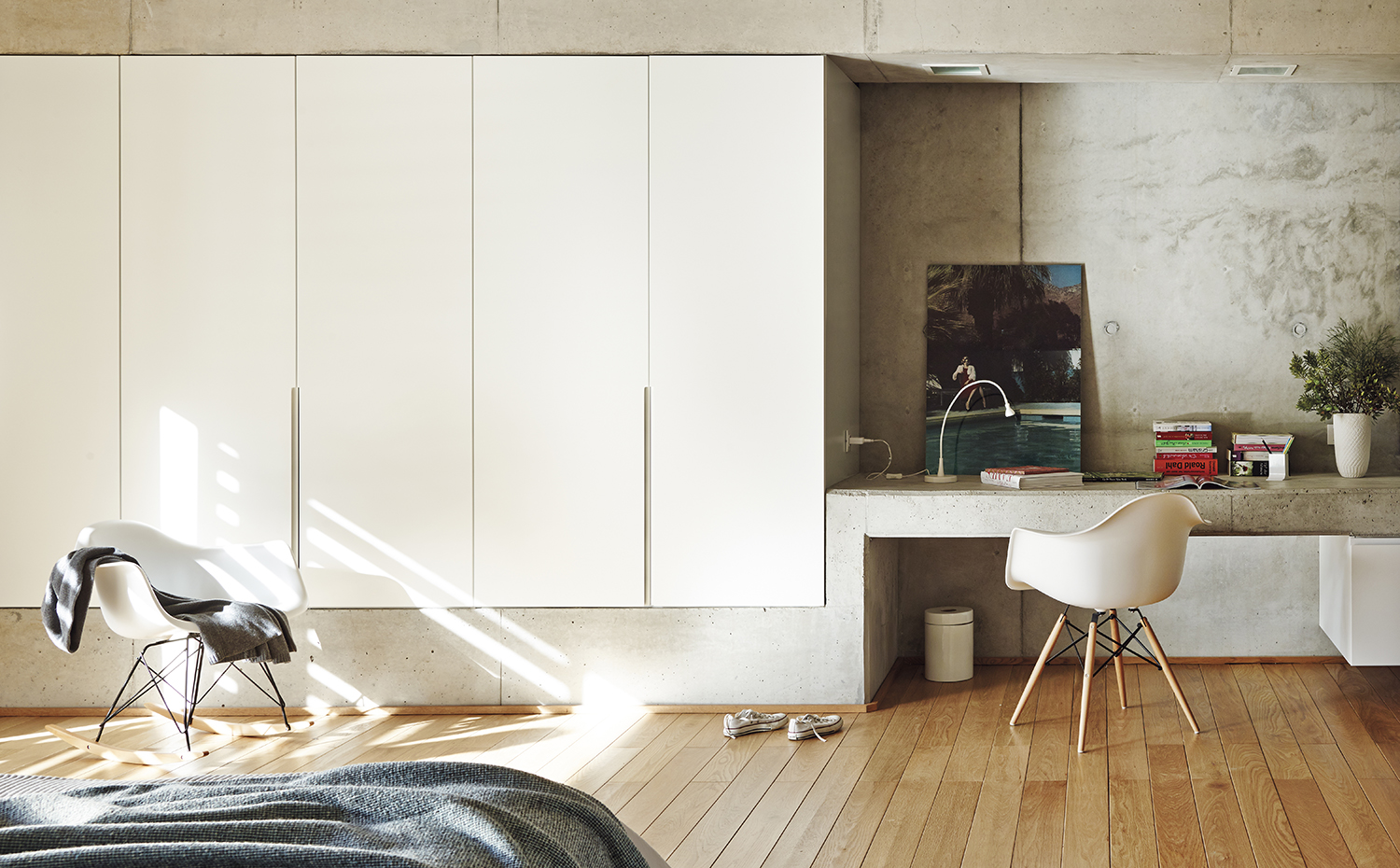 00379480 ok. El armario del dormitorio se encaja en un zócalo de hormigón que zigzaguea para generar la mesa del estudio. Balancín RAR y silla DAW, de los Eames, editadas por Vitra 