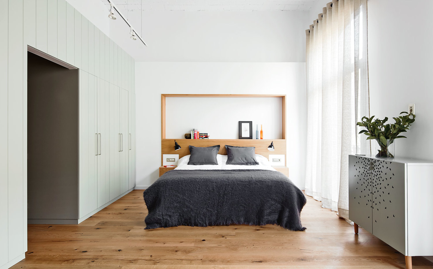REFORMA-CASP-09. El dormitorio, en uno de los extremos de la vivienda, gana intimidad gracias a los armarios de gran capacidad que le dan entrada y a una estructura decorativa de madera hecha a medida a modo de cabezal