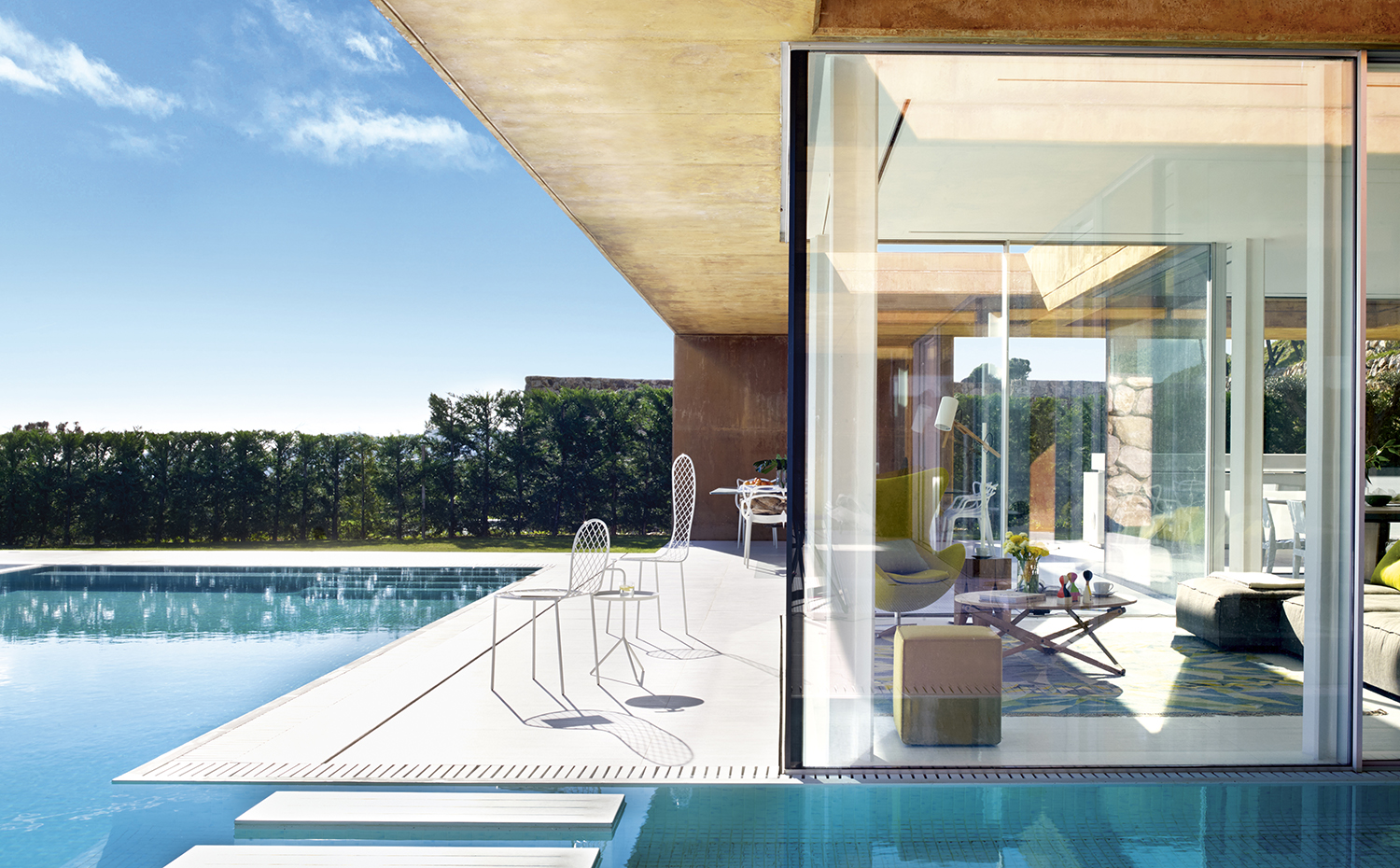 00401214 ok. Para proteger los interiores de la incidencia directa de la luz solar se ha proyectado una pérgola de hormigón de más de treinta metros de largo. Junto a la piscina, dos sillas de la colección Family Chair, de Junya Ishigami para Living Divani, en Minim