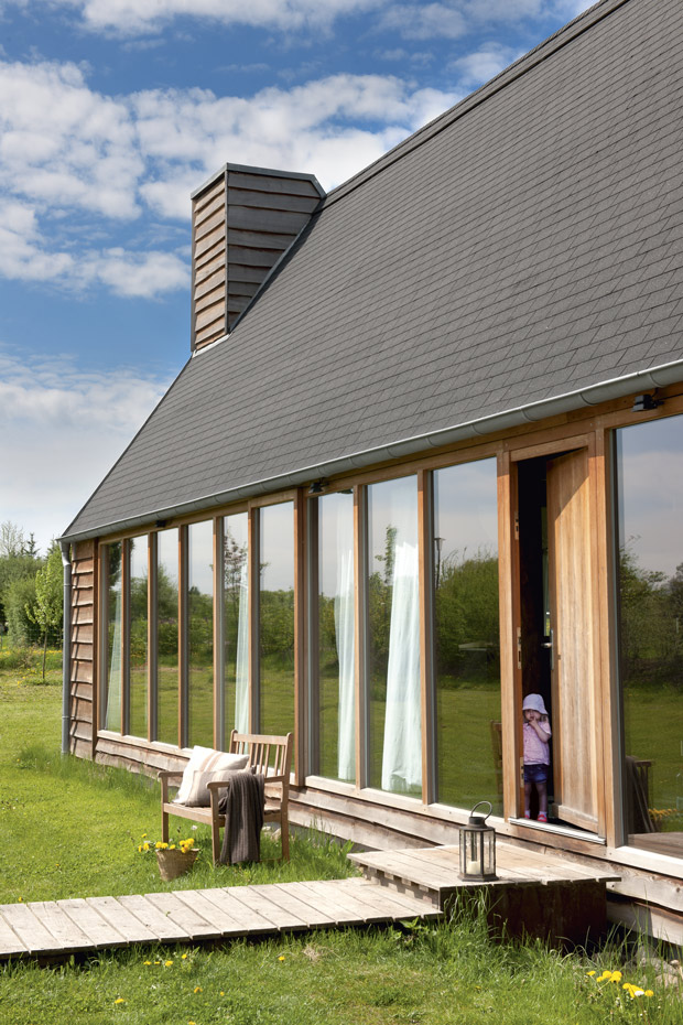 020 DSC6955. La casa es una residencia para pasar las vacaciones. Aparece como si levitara sobre el prado verde, con un techo inclinado negro y una fachada de cristal sobre un pedestal de madera