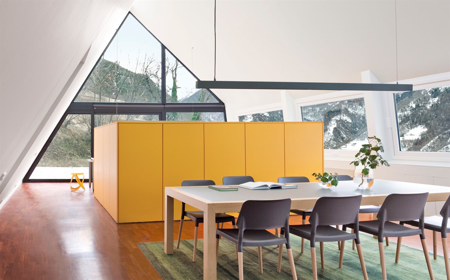 00312482. El mueble-contenedor amarillo separa la cocina del comedor y contiene la escalera de acceso al nivel inferior. La mesa de comedor es de Berna Disseny, hecha a medida por Germans Esteba. Sillas Belloch Chair, de Santa & Cole, en DomesticoShop. Alfombra Blended, de BSB