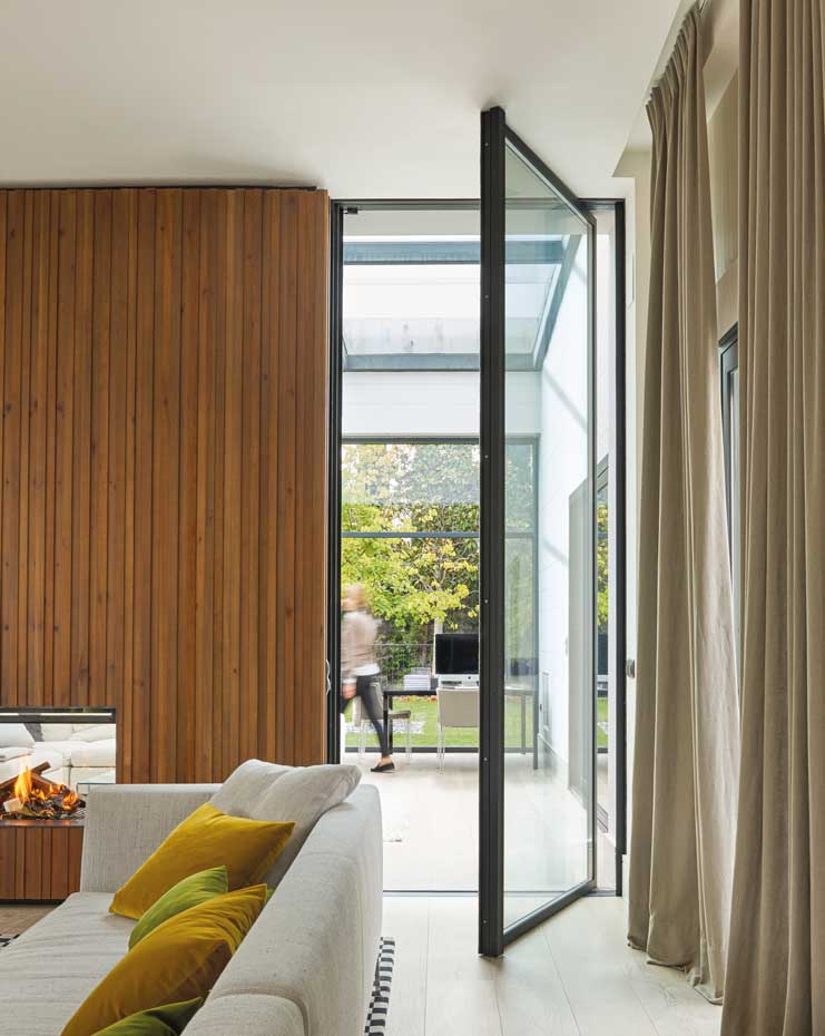 00445712. Una puerta acristalada conduce desde el estar al estudio, abierto a las vistas del jardín y con techo de cristal que introduce la luz natural. Junto al escritorio, una silla de la firma Kartell