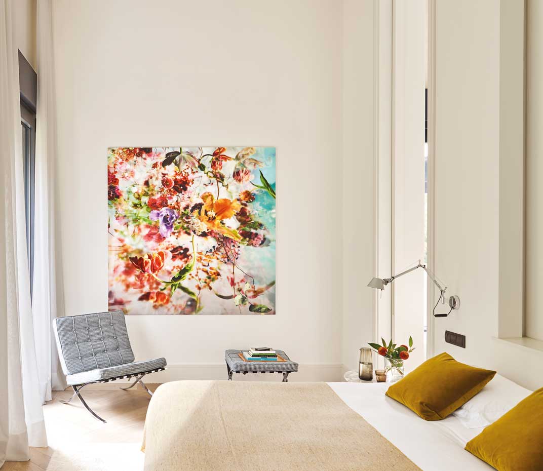 00445722. En la pared, una fotografía con una delicada composición floral, de la artista belga Isabelle Menin. La butaca y el reposapiés son el modelo Barcelona, diseño de Mies van der Rohe que edita Knoll