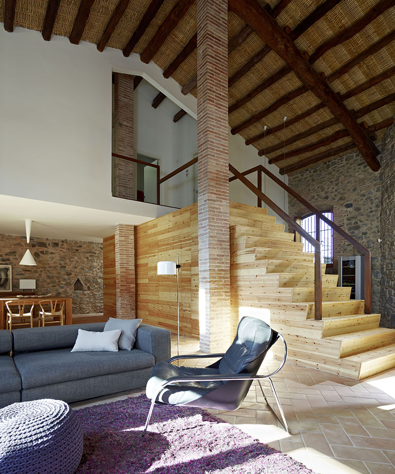 Salón con sofas azules, columnas de ladrillo y escalera de madera.