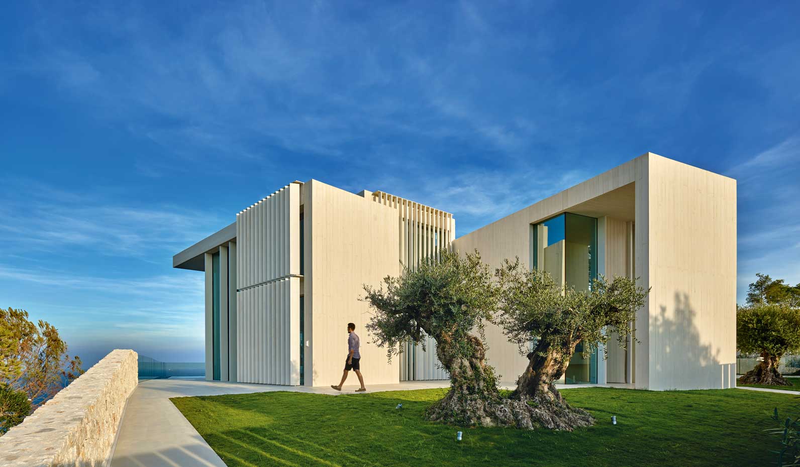 00402405. Mientras que por el lado del mar la casa es abierta y transparente, por su fachada de acceso se muestra hermética y se protege mediante un sistema de lamas verticales orientables y motorizadas de madera de accoya blanqueada