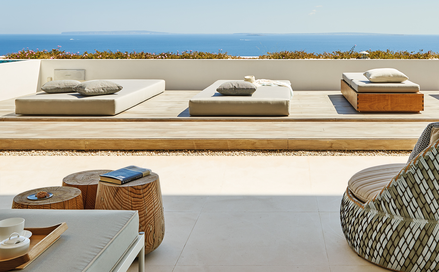 AyD-Saota(Ibiza)2258. Sobre una tarima de madera, camas de día realizadas con madera de iroco y tapizadas, de la firma Okha. Cojines suministrados por St. Leger and Viney, con tejidos de Deco Designs, Black Fabrics y Romo