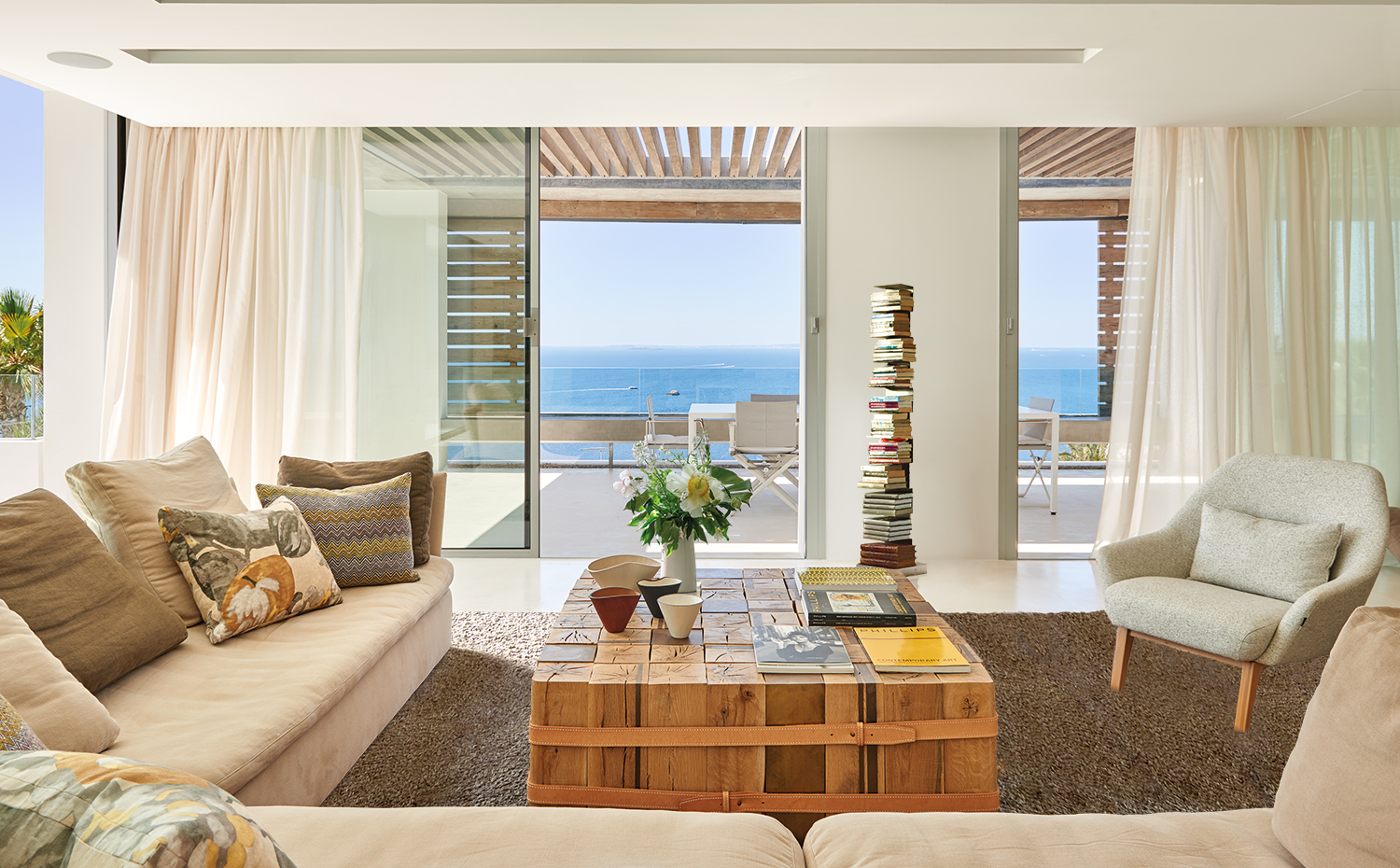 AyD-Saota(Ibiza)2311. Sofá La Plage y butaca Nate, de Okha. La mesa es del mismo fabricante, hecha a medida con roble francés y cuero. Alfombra, de Lignie Design. Encima de la mesa, boles orgánicos de cuero, de la firma Loewe