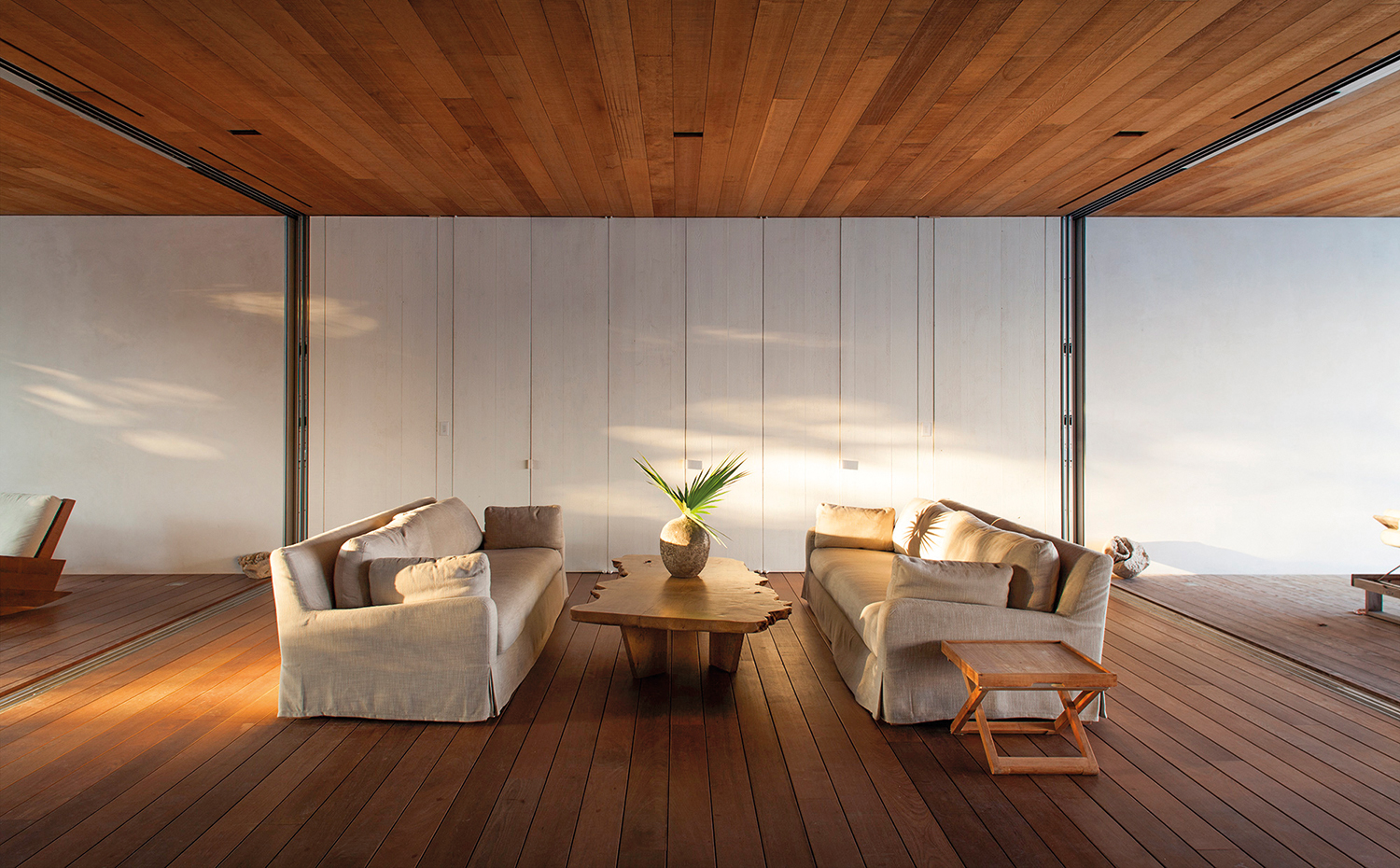 04 House on a Dune MB. Dos sofás idénticos hacen las veces de salón, acompañados de dos mesas en distintos acabados. En la construcción de la casa se han utilizado materiales reciclados como en el caso de la madera de cedro  