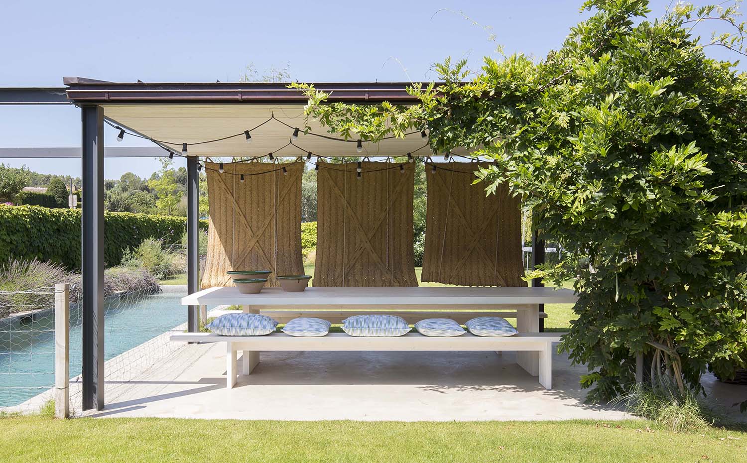 Residencia Ampurdán 8 Bárbara Aurell. Las mesas de centro del porche anexo a la piscina son unos troncos de en madera tropical de El Mercader de Venecia. Los estores de esparto enrollables, inspirados en las masías de la zona, están hechos a medida y proceden de La Bisbal