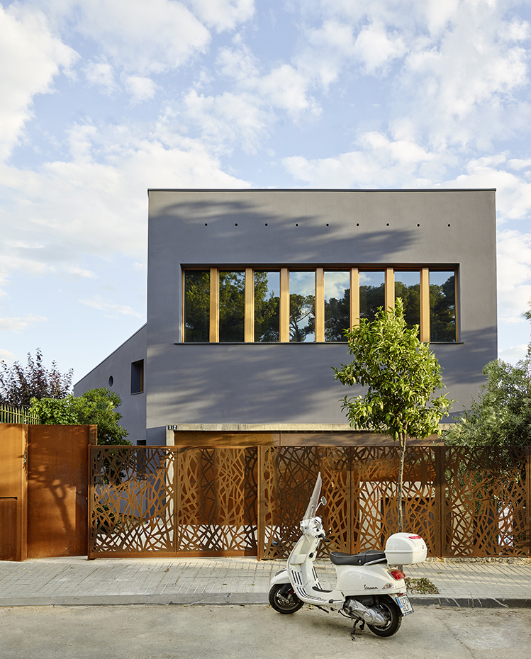 Zest-Vu.Creueta-01 ©Eugeni Pons. La fachada está revestida con un sistema de aislamiento térmico exterior (SATE) con un acabado gris oscuro. La valla de acero cortén, diseño del estudio, se inspira en las esculturas de los árboles del vestíbulo
