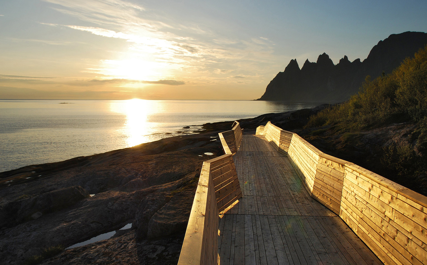 Un sendero diseñado por Code Arkitektur y construido con alerce siberiano discurre por encima de las rocas y ofrece vistas de los escarpados acantilados de Oskhornan, en la ruta de Senja