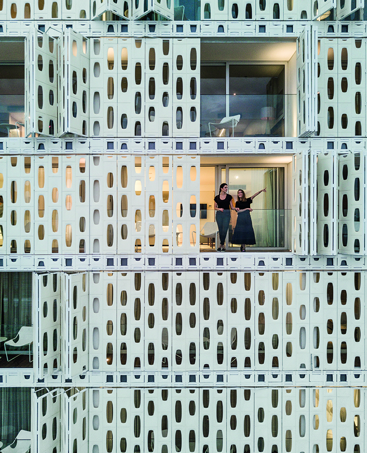 Los paneles perforados de la fachada se abren como puertas plegables desde los balcones de las habitaciones
