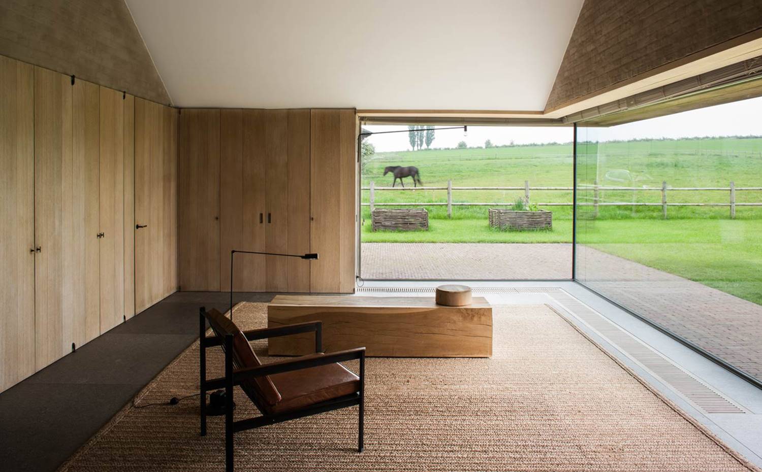 Alfombra de tejido natural, banco de madera y sillón de cuero en esta casa de Vincent Van Duysen.