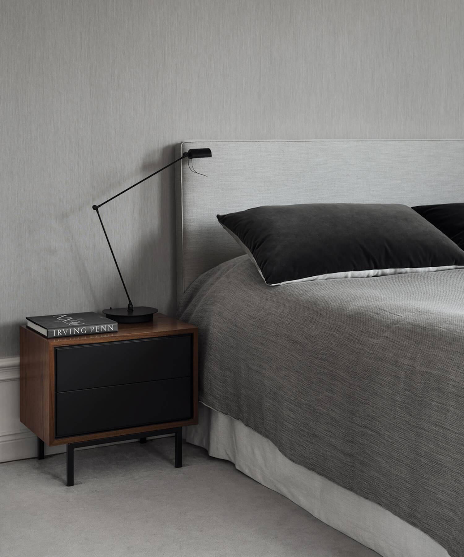 Detalle de un dormitorio en tono gris perla, mesilla de madera y luminaria metálica en negro