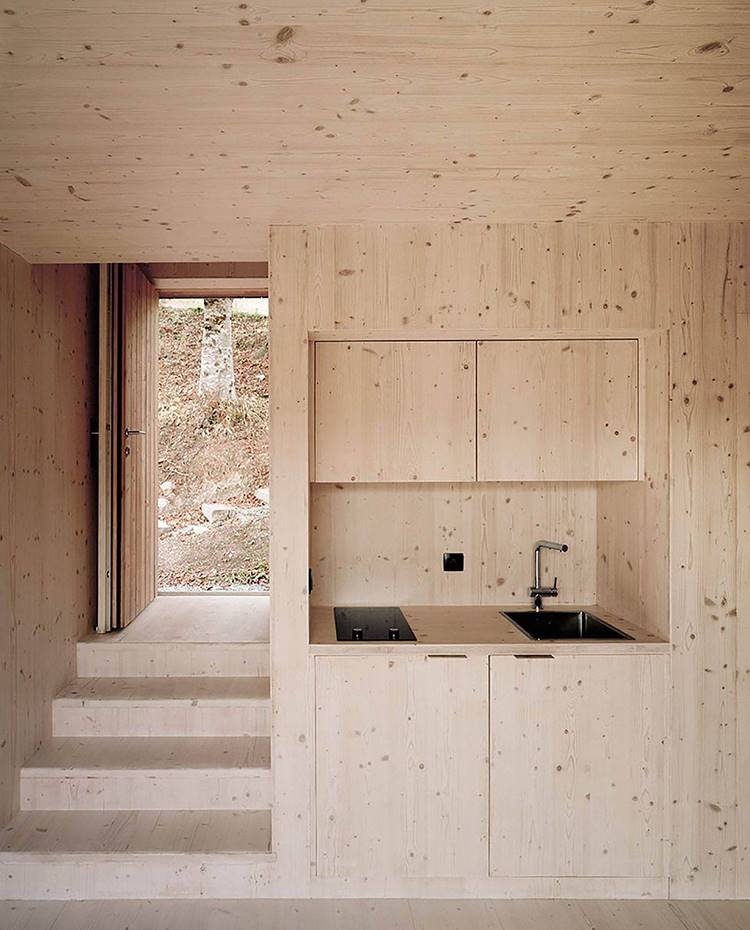pequeña cocina integrada, revestimiento de madera, escaleras a zona de entrada. La cabaña adjunta incluye una coqueta cocina con una pequeña zona de aguas y cocción que se integra por completo en la estética general del proyecto.