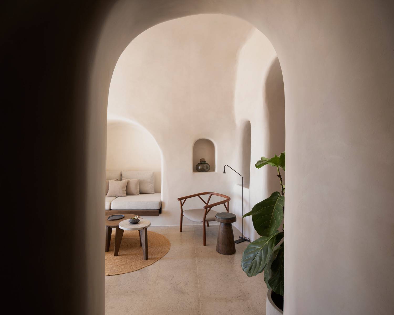 Rincón con sofá, silllas y mesas de una estancia interior de Vora Villas que simula una cueva. Las villas simulan cuevas, con fachadas doradas por el sol e interiores que conservan la temperatura a un ambiente más fresco.