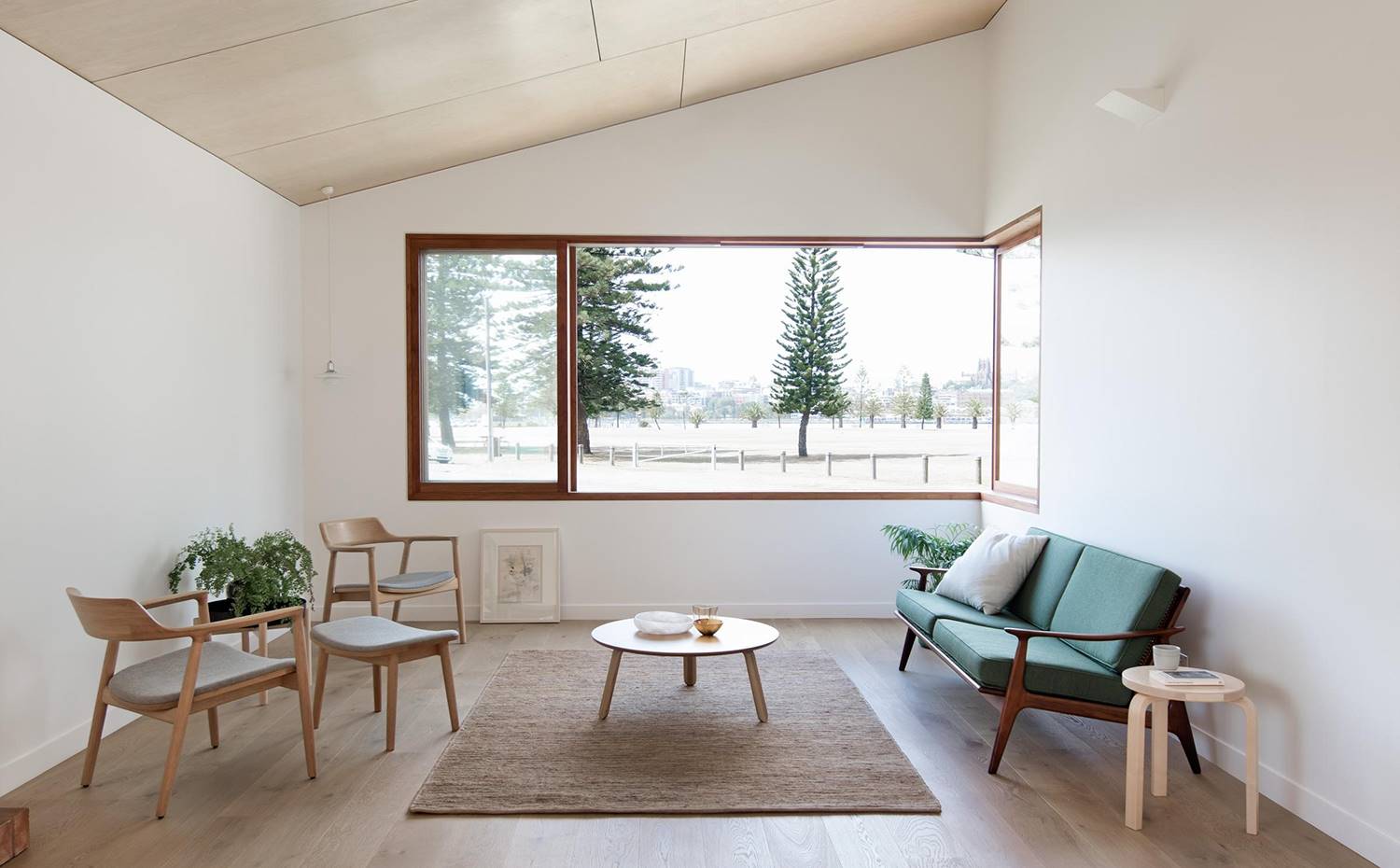 Salón, alfombra bajo mesa comedor, butaca con reposapiés, ventana apaisada, sofá verde. La estética austera se impone en este salón equipado con mobiliario escandinavo 'mid-century'. La gran ventana incluye una repisa para tomar asiento en la propia apertura, proyectándose hacia la zona exterior.