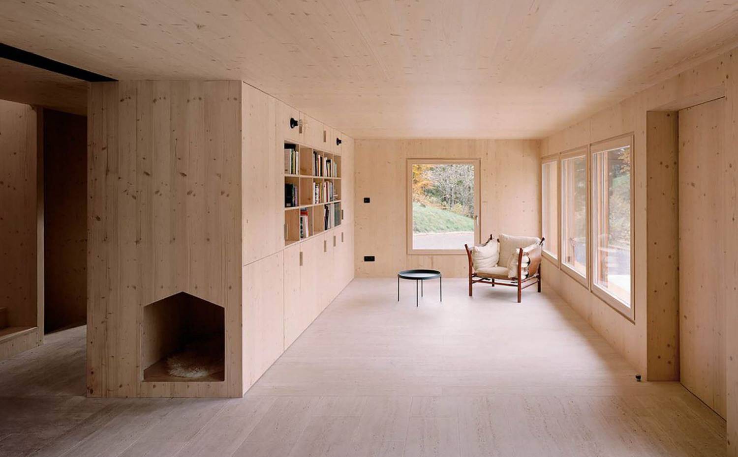salón, librería, butaca rústica, mesita auxiliar metalizada, mobilario de madera, grandes ventanas con vistas. La zona de día incluye esta serena sala de estar donde se imponen un diseño minimalista con una estructura de madera como pieza principal de organización y almacenaje.