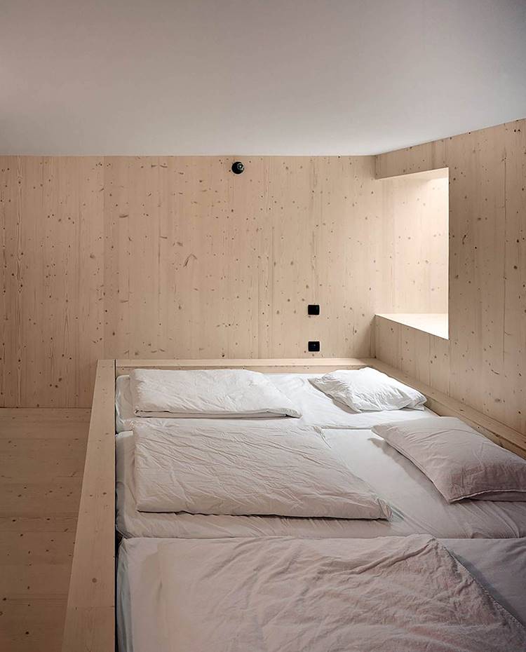 zona de noche cabaña alpina, camas contínuas, tragaluz lateral. Zona de noche situada en la planta superior de la cabaña. Presenta una disposición de camas contínuas y una cálida ambientación dada por la madera y por la estratégica entrada de luz procendente de la ventana y el tragaluz.