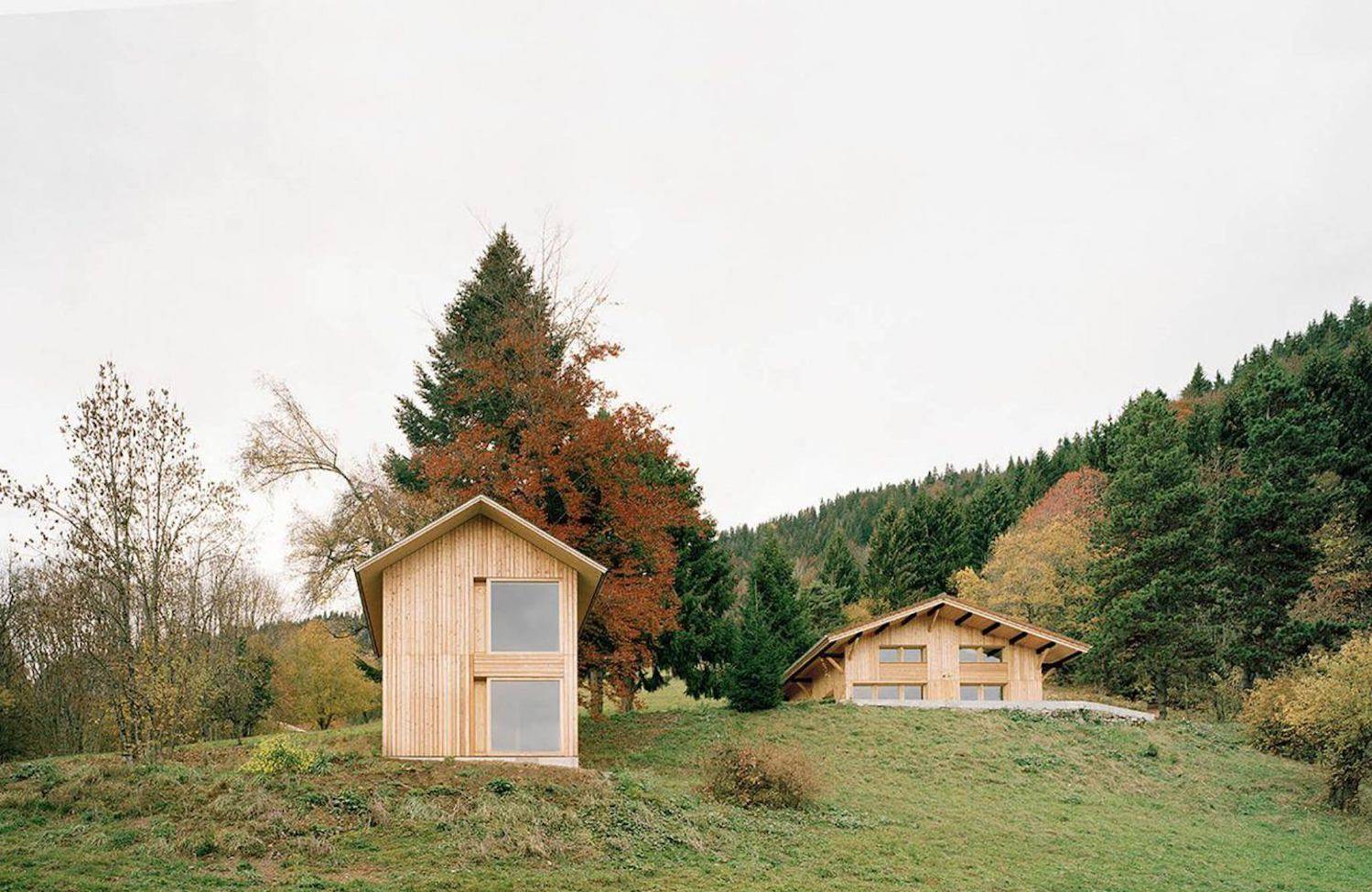 chalet-alpino-exterior-sobre-monticulo-techo-a-dos-aguas-cabana-anexa-revestimiento-de-madera-clara. Inmerso en la naturaleza geniuna de los Alpes franceses, este chalé irrumpe con una estética rompedora de líneas puras, grandes ventanales y el uso de la madera como denominador común en revestimientos, suelos, mobiliario y techos.