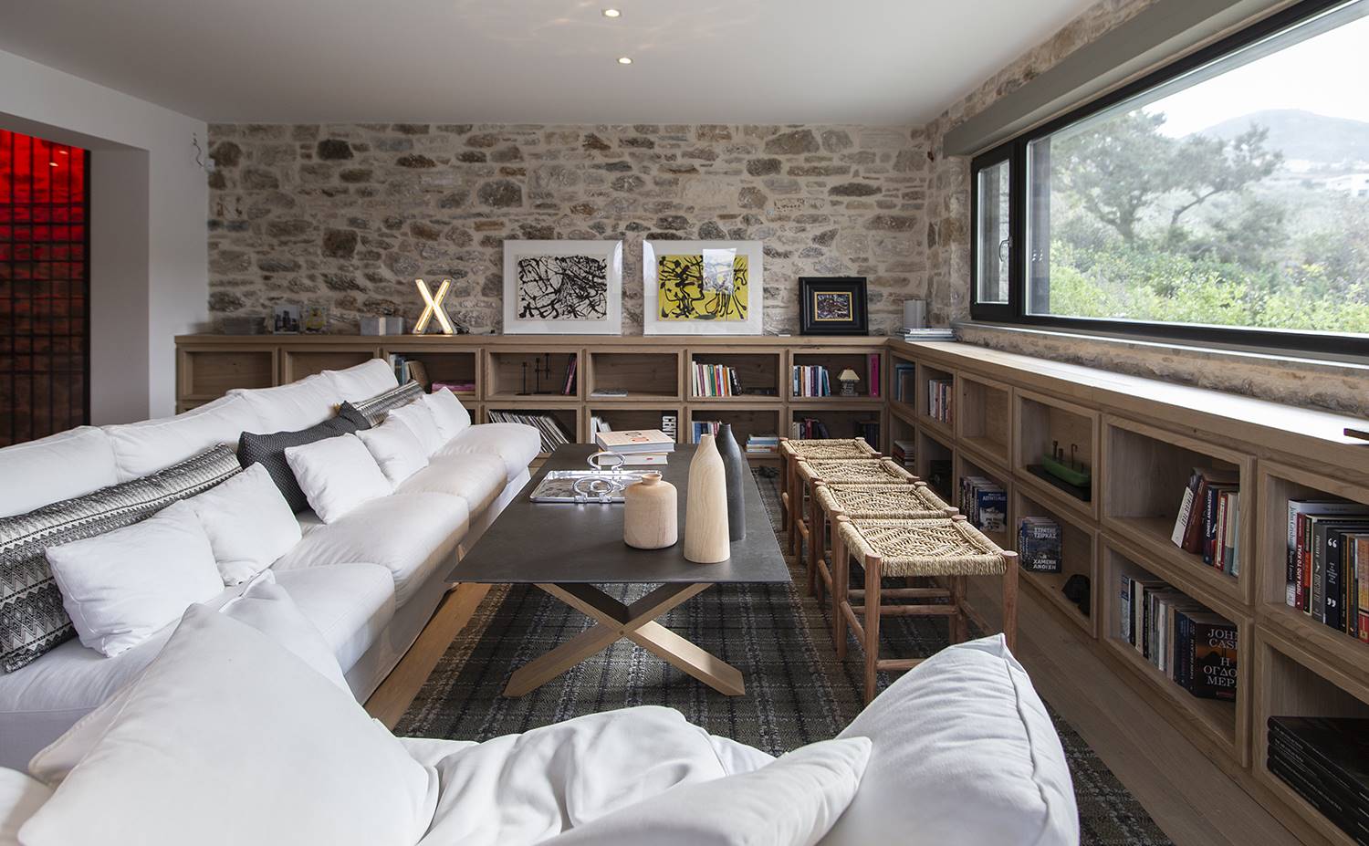 casa kettal grecia 10 salon sofa libreria. Composición de sofás de la marca SITS. La librería es un diseño a medida de Katerina Veremi Xynogala. Mesa de centro de la firma Columbus, con sobre de piedra y patas de roble. Taburetes Anna, de Pomax