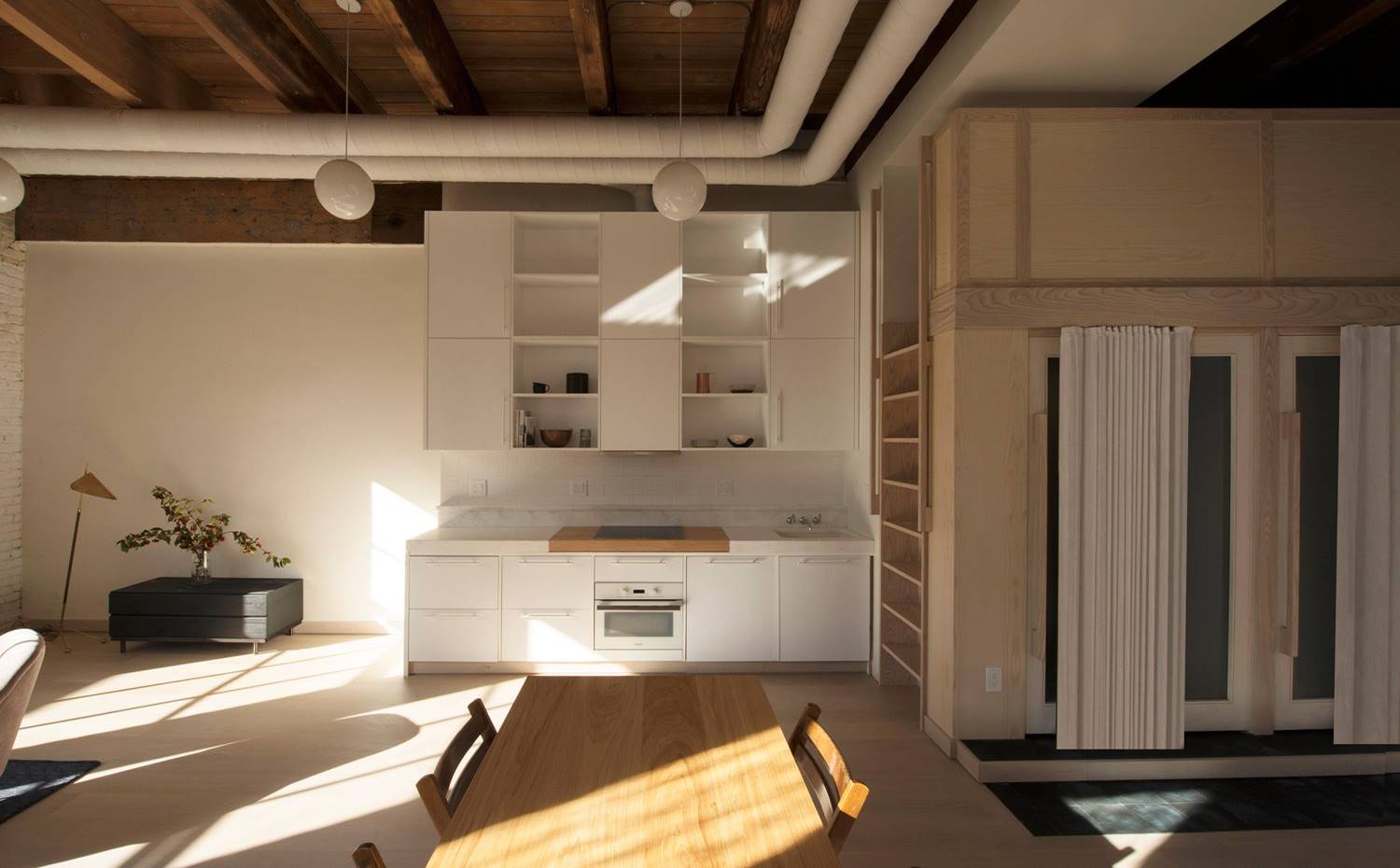 Cocina en línea, mesa comedor madera, estructura de madera con comparitmentos, lámpara de suspensión tipo globo. Dada la gran altura de la vivienda, el dormitorio se encuentra en un entrepiso superior, al que se accede a través de una escalera integrada. 
