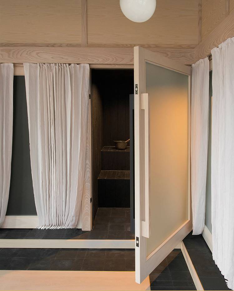 Puerta abatible entrada sauna, estructura de madera, lámpara de suspensión tipo globo,cortinas blancas. Los cerramientos de cada uno de los espacios se ha realizado con estructuras de madera de roble y cristal esmerilado. Y para una mayor privacidad y  sugerencia, se acompaña de cortinas blancas. 