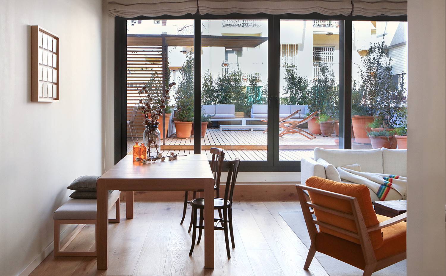 Comedor, mesa de madera, bancada, exterior patio interior, butaca madera, sofá blanco. Tanto la sala de estar como los dormitorios se abren por completo a la terraza consiguiendo gran amplitud visual. La dominante cromática de tonos neutros que impera en la zona de día permite que la vegetación exterior focalice la atención.