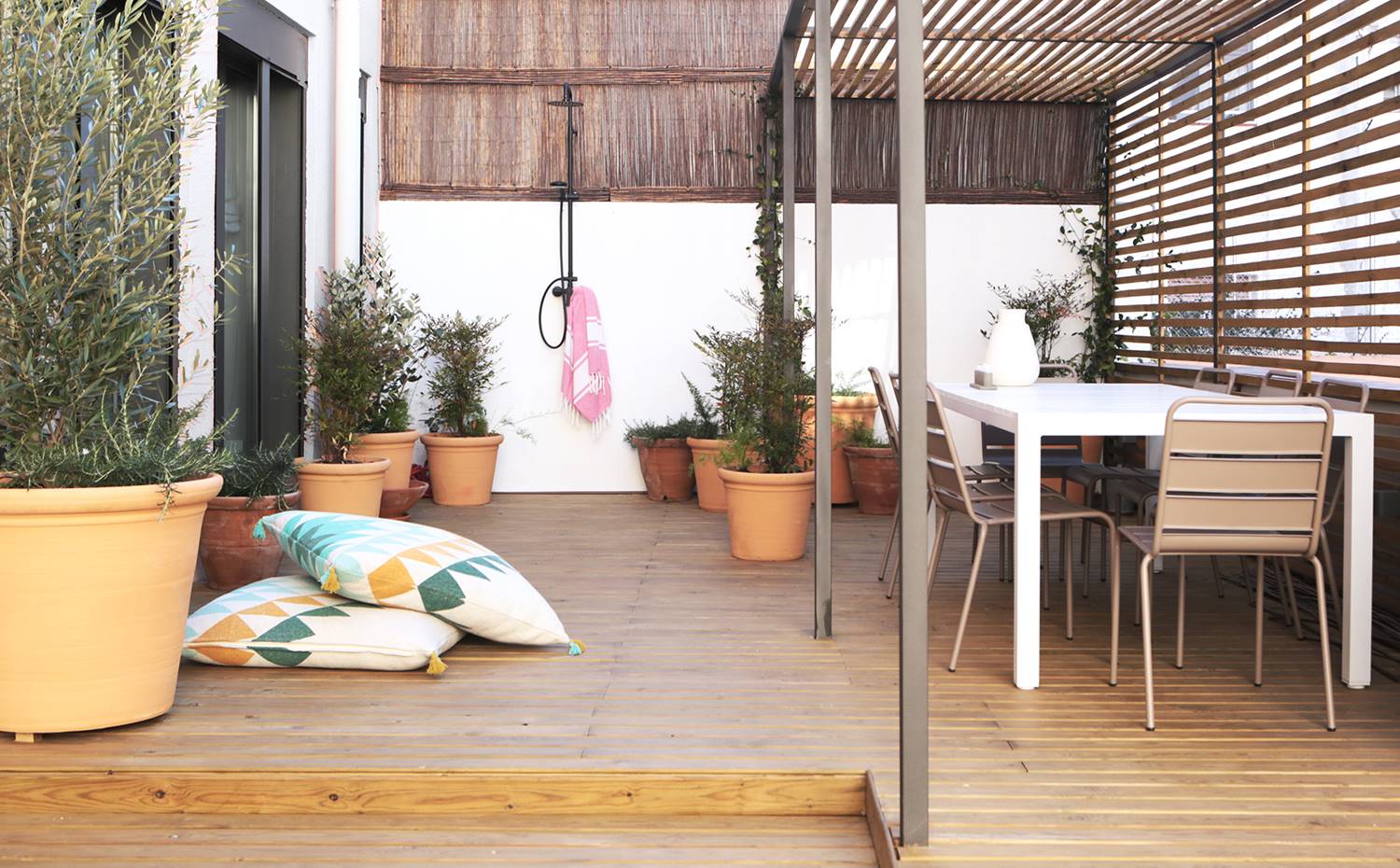 Patrio interior con celosía, mobilario exterior, mesa comedor blanca, gran macertero arbol. La terraza exterior, verdadera joya de la casa, se ha tratado con celosías de antracita y vidrio acanalado para jugar con la ventilación, la luz y la privacidad.