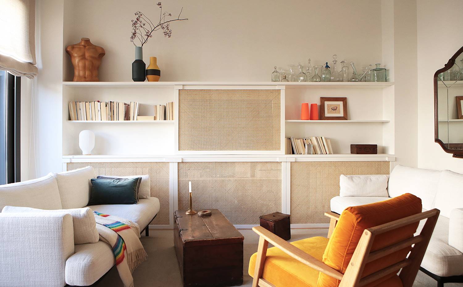 Salón, sofá blanco, butaca madera, estanteria de obra, cerramientos regilla vegetal. La rejilla vegetal se convierte en un elemento común en las diferentes estancias adoptando diferentes funciones. En el salón, se ha empleado para el mueble hecho a medida que integra una librería y oculta el televisor y otros aparatos electrónicos.