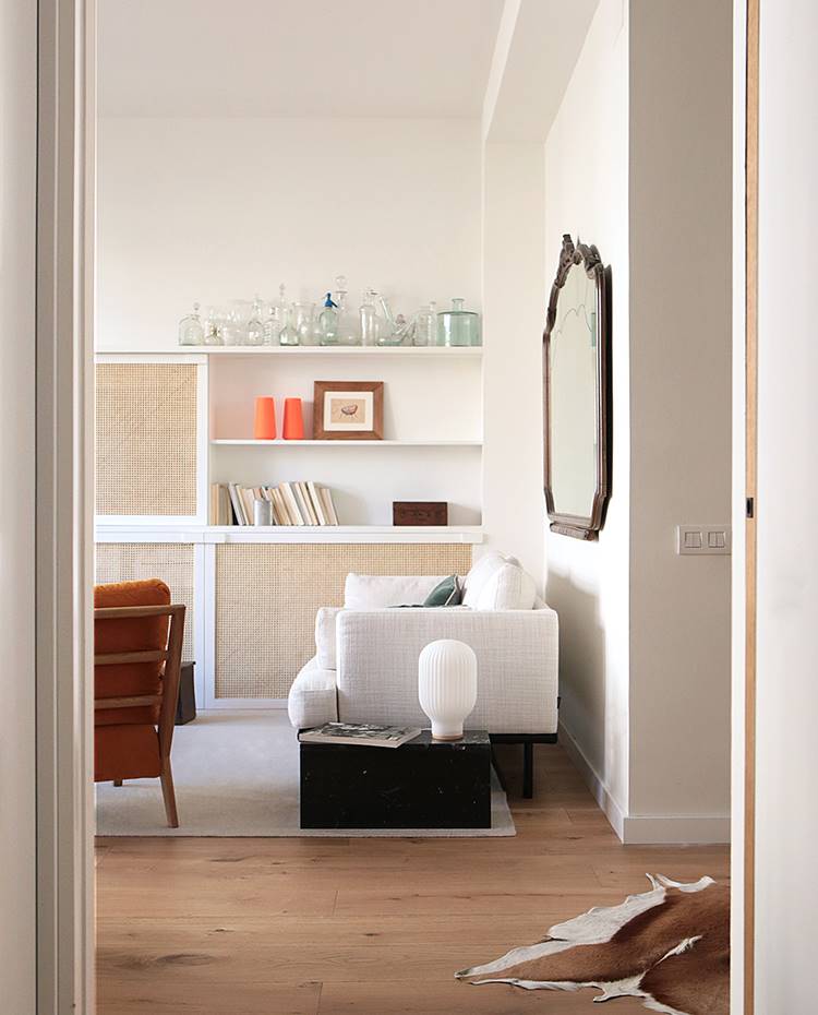 Sofá blanco, espejo vintage en pared blanca, baúl auxiliar, suelo madera. La propietaria también tenía piezas antiguas de gran valor sentimental pertenecientes a su madre que se han ido integrando en los diferentes espacios. 
