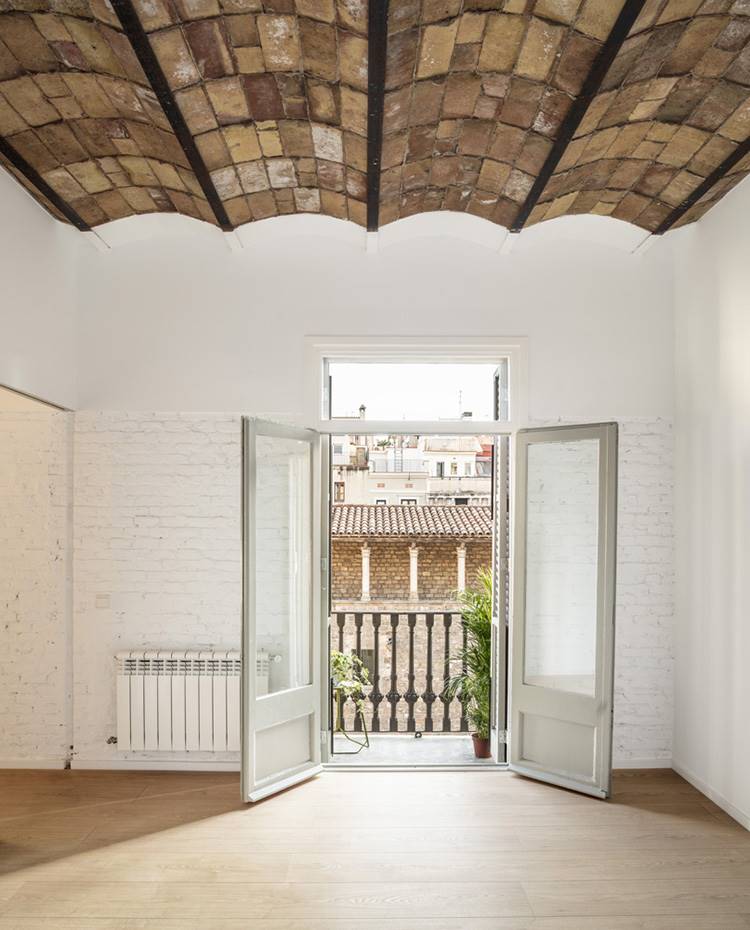Balcón abierto, pared ladrillo visto, techo con volta catalana. La vivienda cuenta con tres balcones que asoman al casco histórico de Barcelona, uno de ellos situado en el dormitorio continuo al comedor, provisto de gran claridad gracias a su dominante color blanco solo interrumpido en techos y suelos.