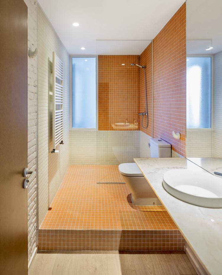 Baño, ducha de obra, lavamanos encastrado en encimera, gresite naranja. Toques de color naranja tiñen los baños de la casa jugando con un doble criterio: estético y funcional. Se levantó la zona de sanitarios y ducha para pasar las instalaciones de saneamiento y lograr un efecto singular y atractivo.