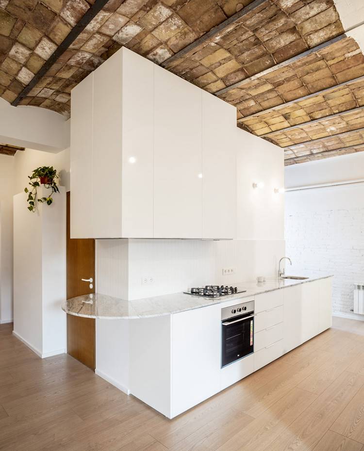 Cocina blanca en línea, zona de fuego en acero, encimera mármol. La cocina abierta ocupa una posición central en el proyecto llevado a cabo por el estudio de arquitectura CRÜ. Dominantemente blanca, se organiza en forma de L entorno a un cuarto de baño continuo.