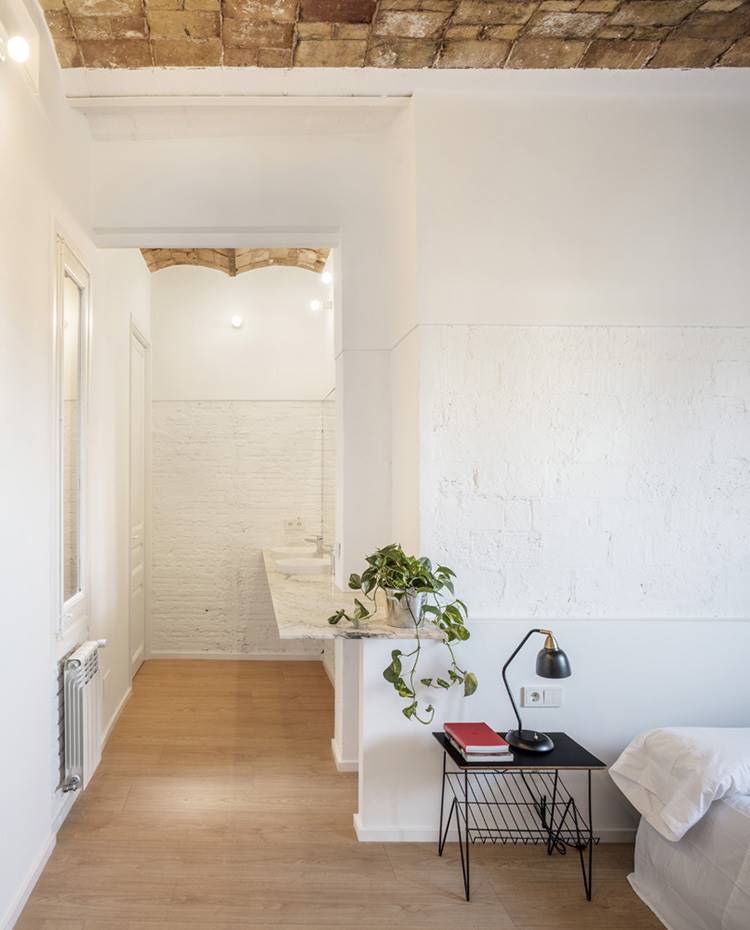 Dormitorio, estante a medida de mármol, mesita negra, lámpara de sobremesa negra. En el dormitorio (casi) todo parece apostarse al blanco, a excepción de la mesita auxiliar y la luminaria de sobremesa que ponen el contrapunto en negro. Se ha habituado un estante de obra hecho de mármol blanco.