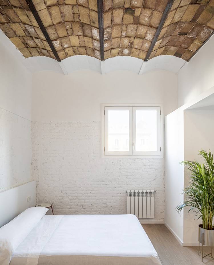 Dormitorio, ventana exterior, vegetación interior, techo con volta catalana. El dormitorio actúa como un lienzo en blanco donde el foco parece dirigirse hacia el techo donde se ha recuperado la tradicional y sugerente bóveda catalana.  