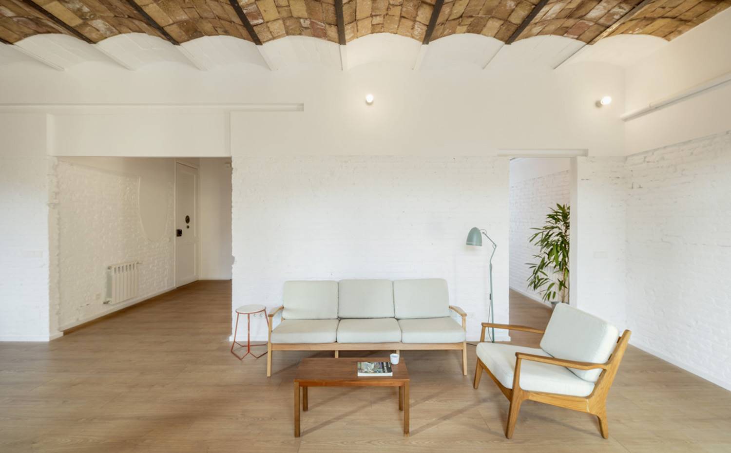 Sala de estar diáfana, sofá blanco, butaca blanca, mesita auxiliar de madera. Piezas etéreas visten el amplio salón, en sintonía con el binomio madera y blanco que impera en el proyecto, Comparte espacio con el comedor en medio de una estructura totalmente despejada de artificios.