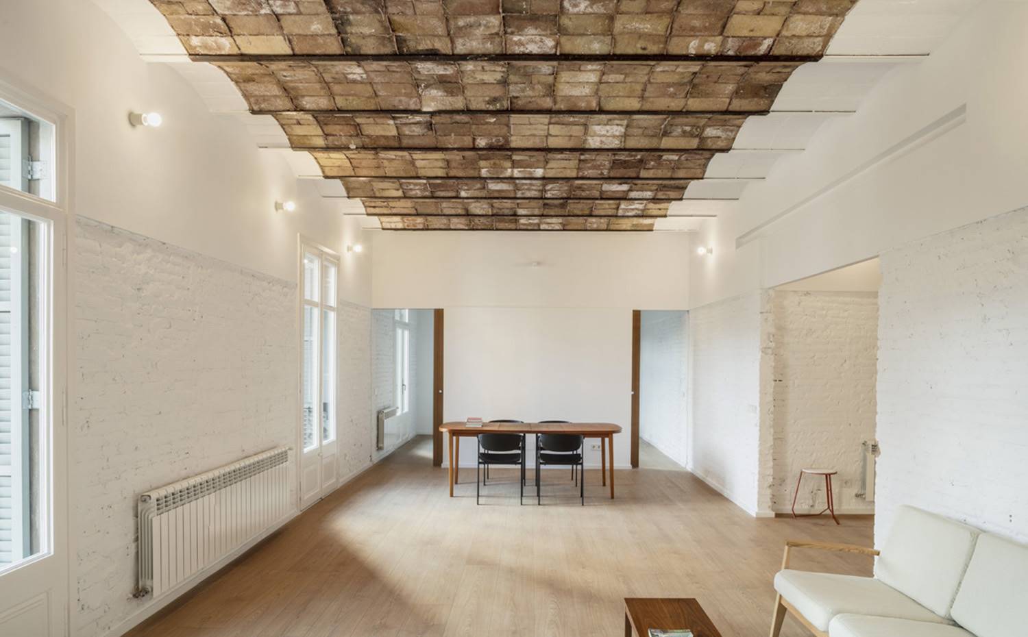 Salón y comedor, puertas con acceso a dormitorios, espacio diáfano, techo con volta catalana. El comedor se enmarca entre las dos puertas correderas que dan acceso a uno de los tres dormitorios con los que cuenta la vivienda. Goza de una gran entrada de luz natural procedente de los tres balcones que se abren a la calle.