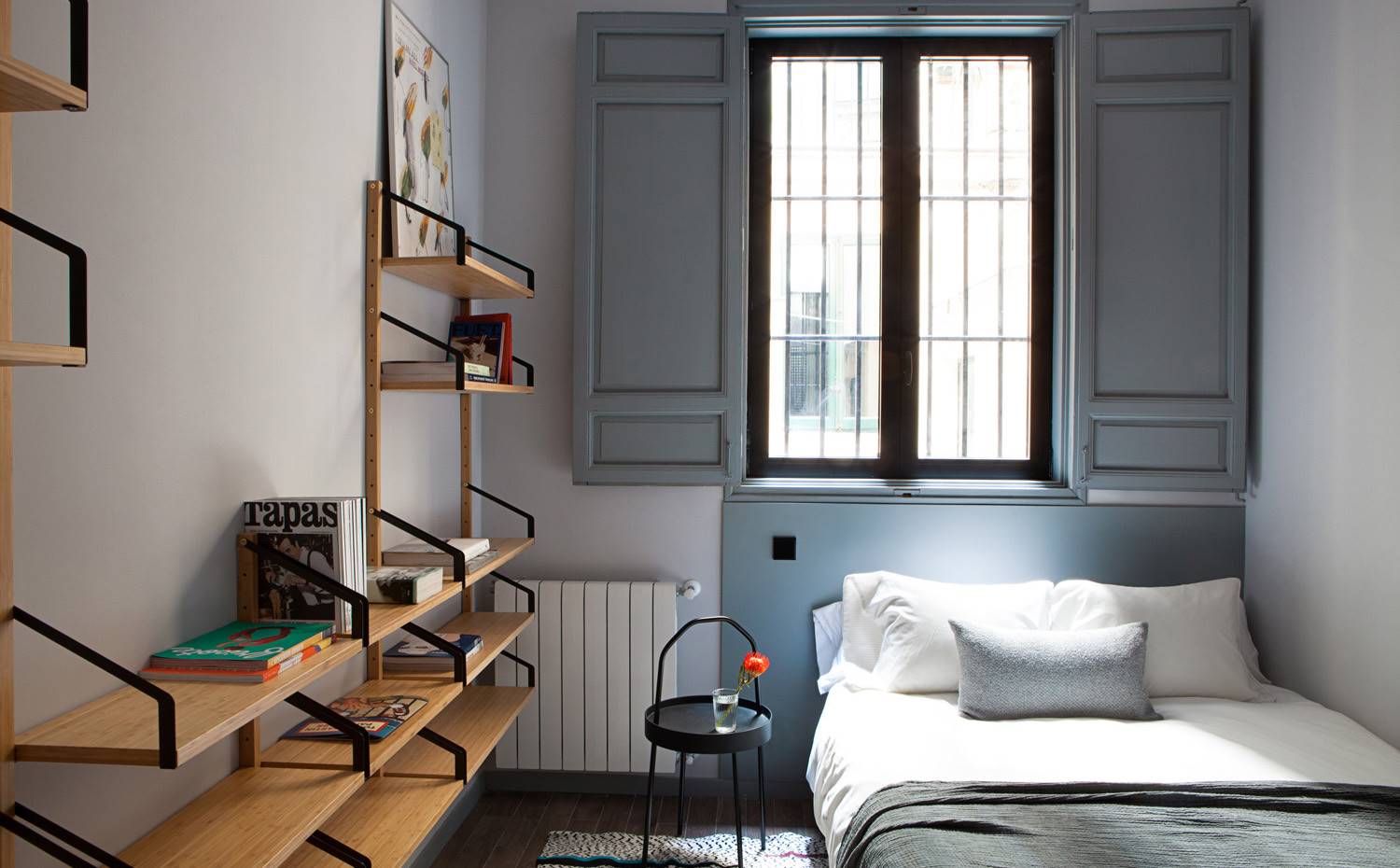 Estantes de madera a dispuestos en pared a modo de librería, ventana con cerramientos de madera. En esta habitación todo es similar a la madera. Originariamente era la habitación más fría del apartamento, puesto que da a un patio, por lo que ha necesitado ser tratada para resultar lo más acogedora posible