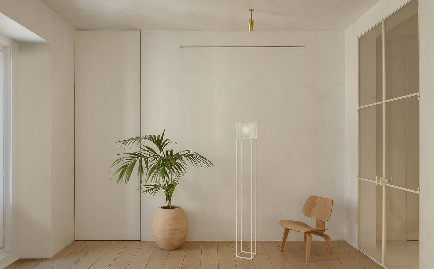Puerta de acceso, vestíbulo, planta con jarrón suelo terroso, suelo de madera, puerta acristalada, silla decorativa. Para la reforma de esta vivienda se tiraron abajo las divisiones interiores originales a fin crear estancias más amplias y diáfanas donde la luz natural penetrara y circulara por el espacio.